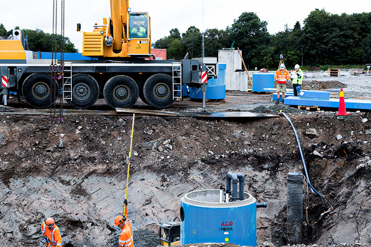 En byggarbetsplats med byggarbetare, kranbil och blå betongtank..