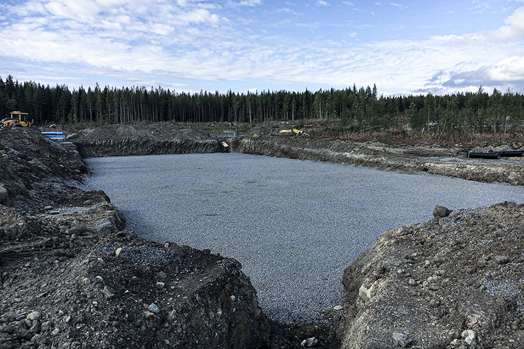 Byggarbetsplats med grusbelagd markyta framför skog.