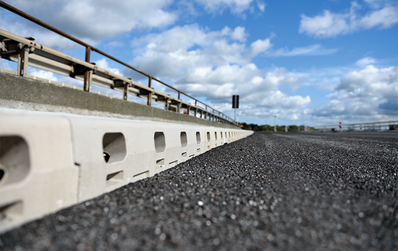 Väg av asfalt med grå betongrännor och räcke.