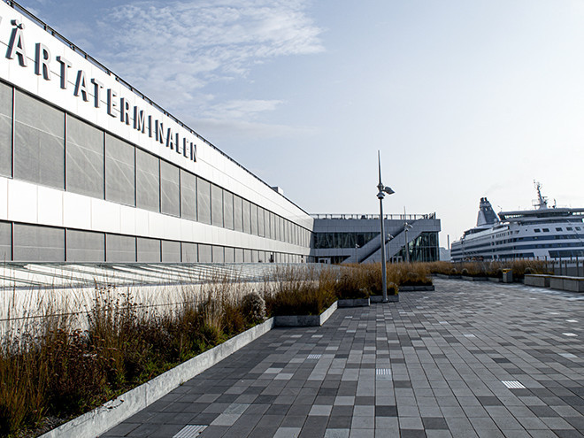 En stor vit byggnad vid hamnterminalen, med en färja i bakgrunden.