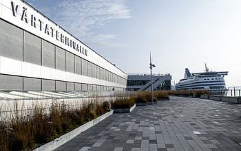 En stor vit byggnad vid hamnterminalen, med en färja i bakgrunden.