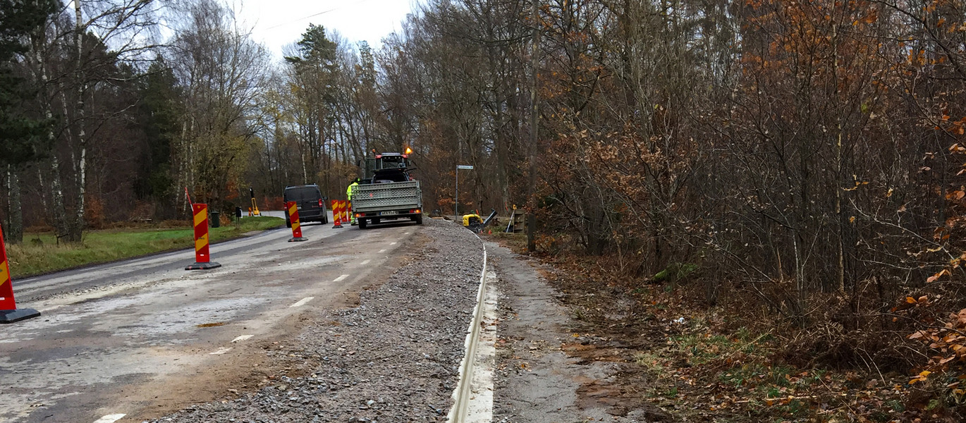 Vägen är avspärrad och en traktor med släp står parkerad.