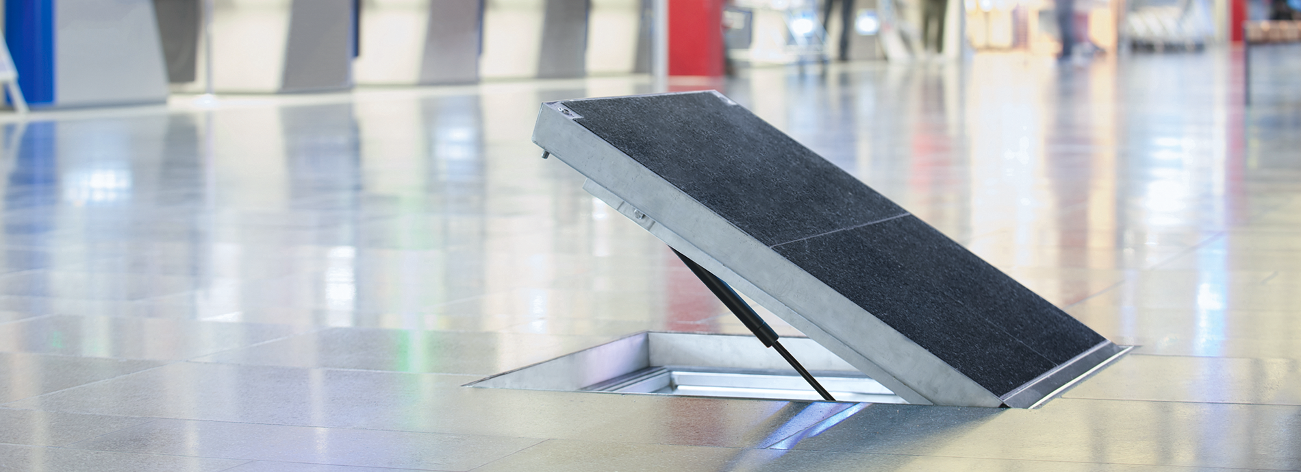 Halvt öppen golvlucka med svart ovandel.