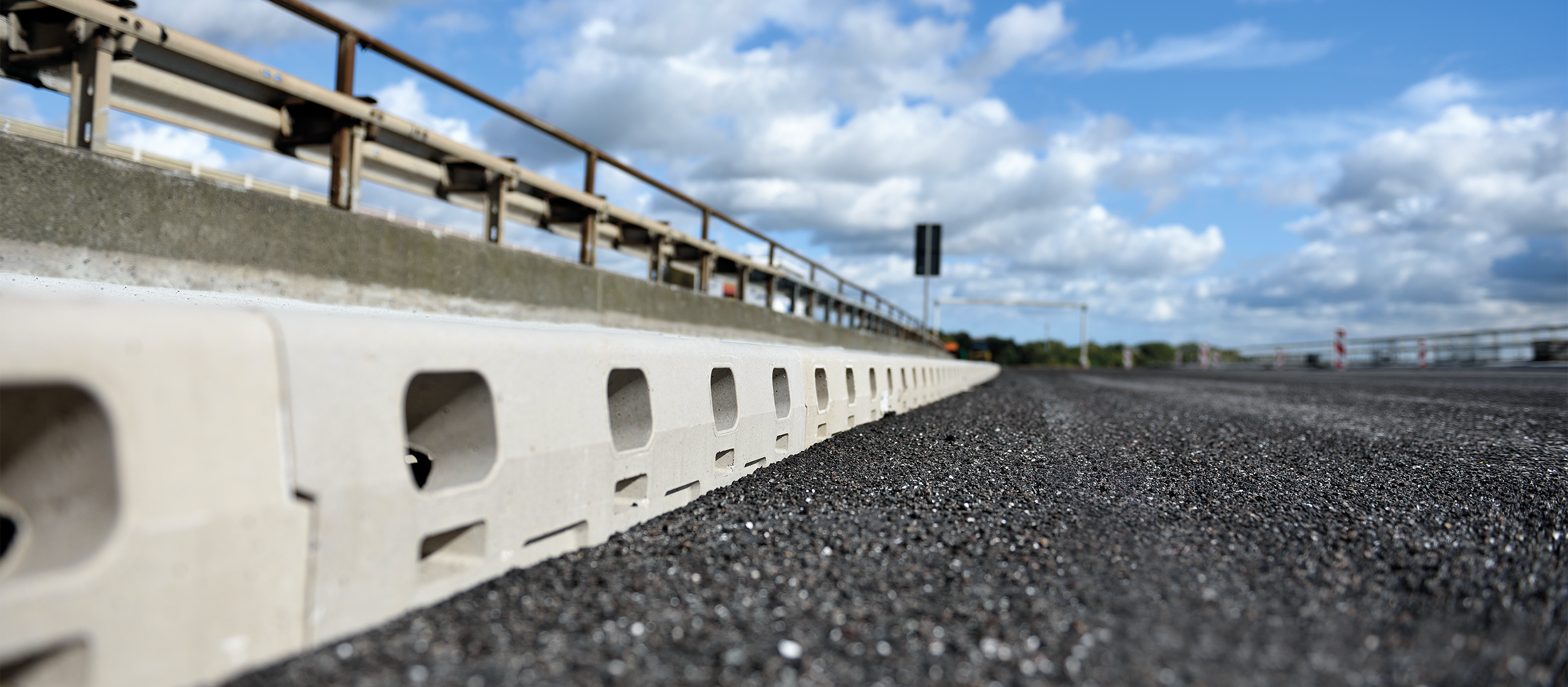 Väg av asfalt med grå betongrännor och räcke.