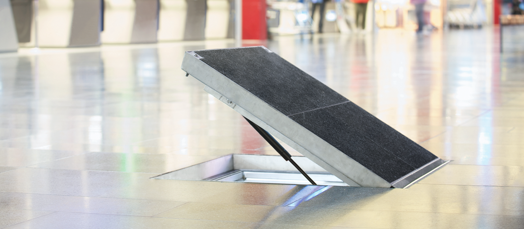 Halvt öppen golvlucka med svart ovandel.