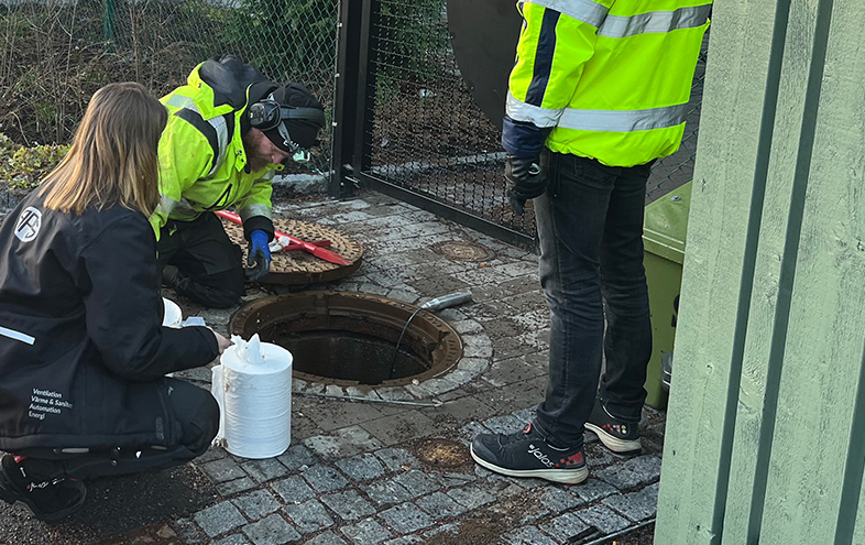 Två män i gula säkerhetsjackor arbetar och förevisar en kvinna brunnen.